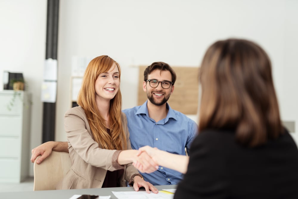 Happy young couple meeting with a broker in her office leaning over the desk to shake hands, view from behind the female agent-Oct-18-2024-05-43-21-0988-AM